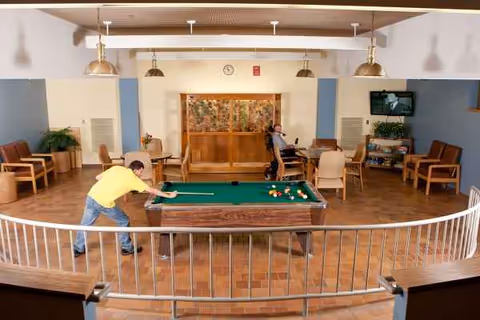 Indoor common area with a billiards table and residents playing a game.
