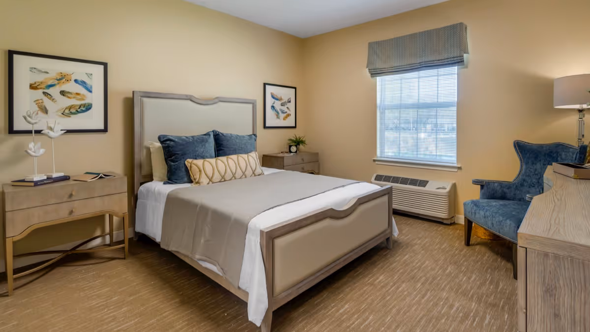 Furnished bedroom with a bed, two nightstands, an upholstered armchair, and a window.