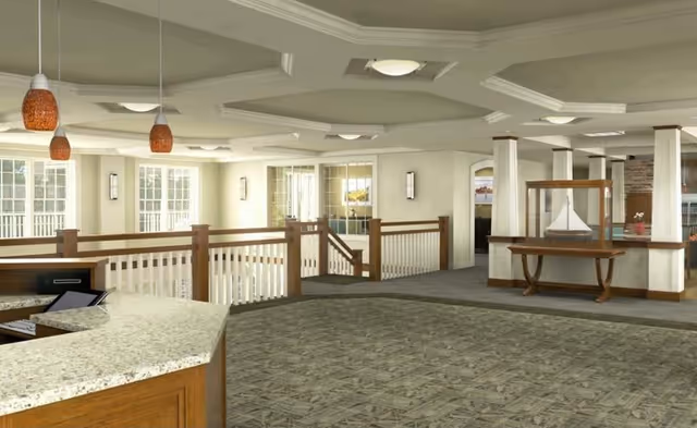 Spacious interior area with carpeted floor, wooden railing around a stairwell, large windows letting in natural light, and a display case with a model ship. The ceiling has decorative molding and recessed lighting, and there is a granite countertop visible in the foreground.