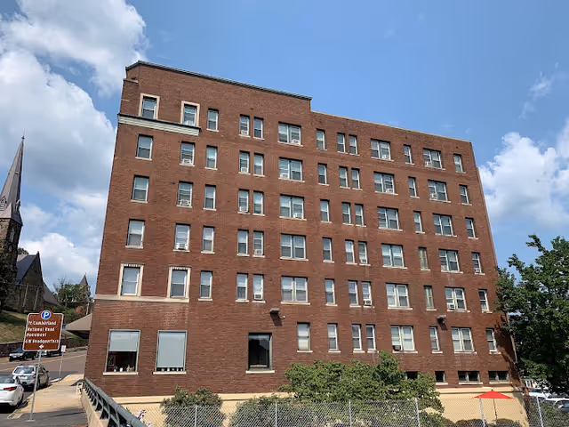 Brick multi-story senior living building with many windows against a blue sky.