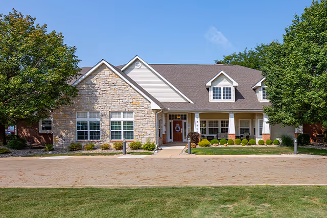 Single-story senior living building with stone facade, entryway, and landscaped front yard.