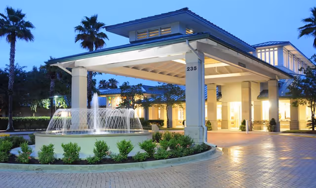 Entrance of Westminster St. Augustine facility at dusk with a covered drop-off area, illuminated fountain, palm trees, and well-maintained landscaping.