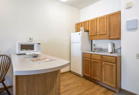 Compact kitchen area with wooden cabinets, refrigerator, microwave, and curved island.