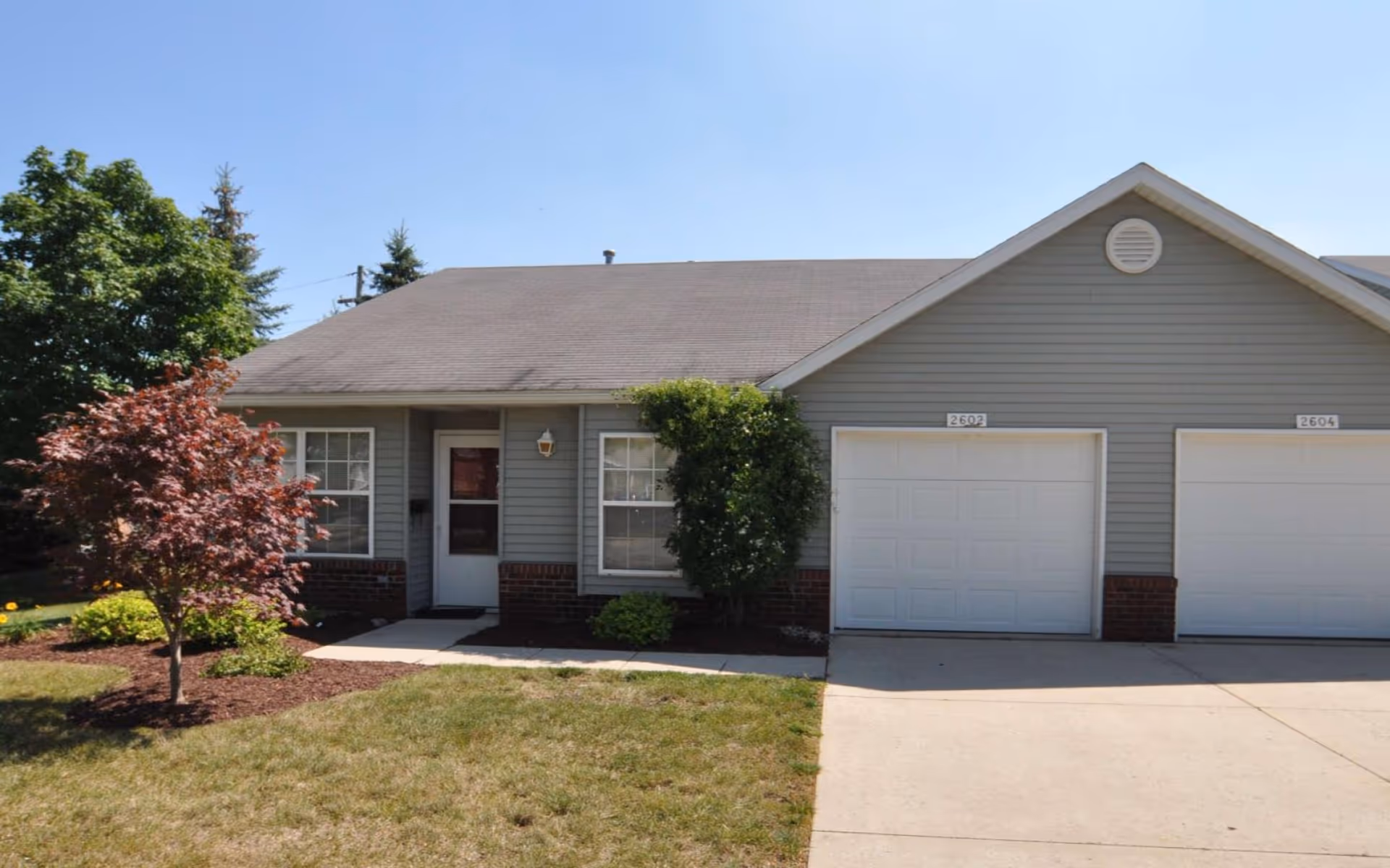 Single-story attached townhouse with two garages, a front door, and a small landscaped yard.