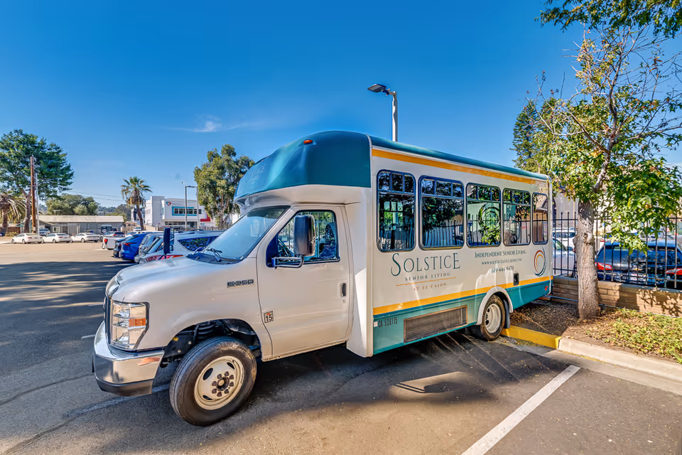 A Solstice Senior Living shuttle bus parked in a sunny parking lot next to trees.