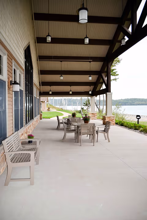 Covered lakeside patio with tables, chairs and benches under a timber-beamed roof next to a building.