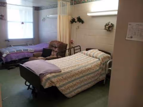 Two hospital-style beds in a shared bedroom with a chair and curtains.