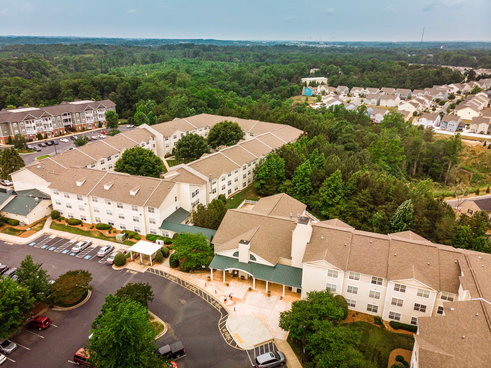 Aerial view of The Dorchester senior living complex showing multi-wing buildings, parking areas, and surrounding trees.