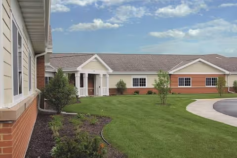 Exterior view of RidgeStone Terrace facility with green lawn, shrubs, and a curved sidewalk.