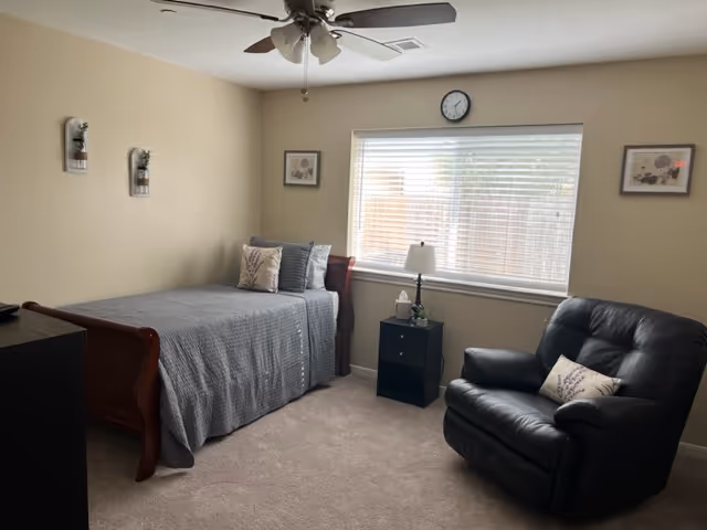 Bright senior living bedroom with a bed, leather chair, nightstand, and window.