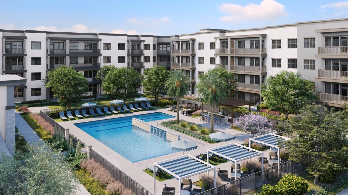 Outdoor courtyard area of a senior living facility featuring a large swimming pool with lounge chairs and umbrellas, surrounded by landscaped greenery, palm trees, and a multi-story residential building with balconies in the background.