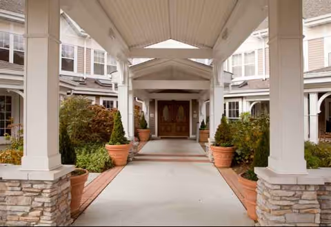 Covered walkway to Sunrise entrance with white columns, potted plants, and double doors.