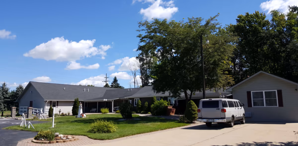 Sandalwood Creek senior living facility exterior with manicured lawn, trees, and a parked white van.