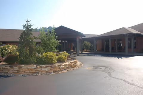 Exterior view of Elison Assisted Living & Memory Care of Marietta showing the entrance with a covered driveway, landscaped greenery with bushes and a small tree, and a paved driveway.