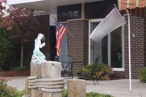 Exterior view of Dunkirk Rehabilitation and Nursing Center with flag, statue, and entrance.