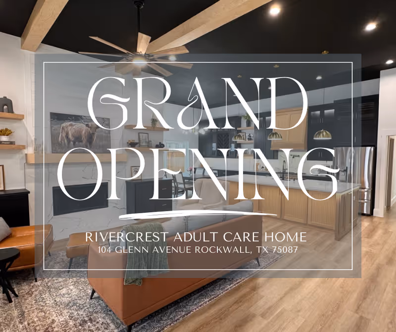 Modern open living room and kitchen area with a brown leather sofa, armchair, fireplace, ceiling fan, and wooden flooring. The kitchen features black and wood cabinetry, stainless steel appliances, and pendant lighting.