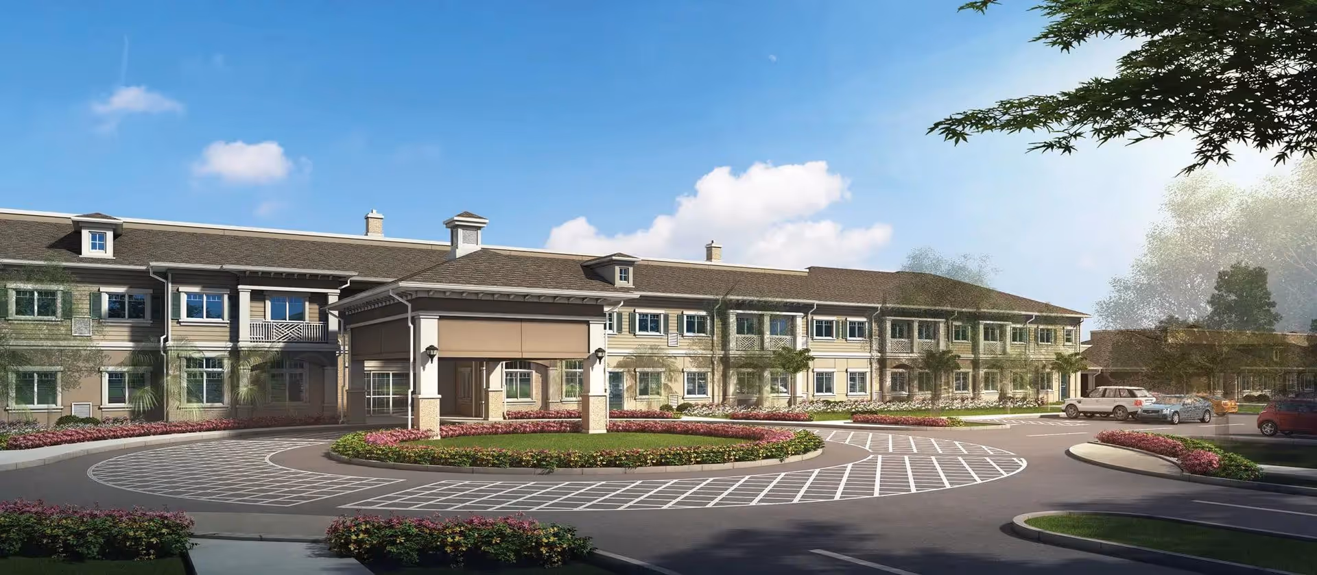 Exterior view of a two-story senior living facility building with a covered entrance, surrounded by landscaped flower beds and a circular driveway with parked cars under a blue sky with some clouds.