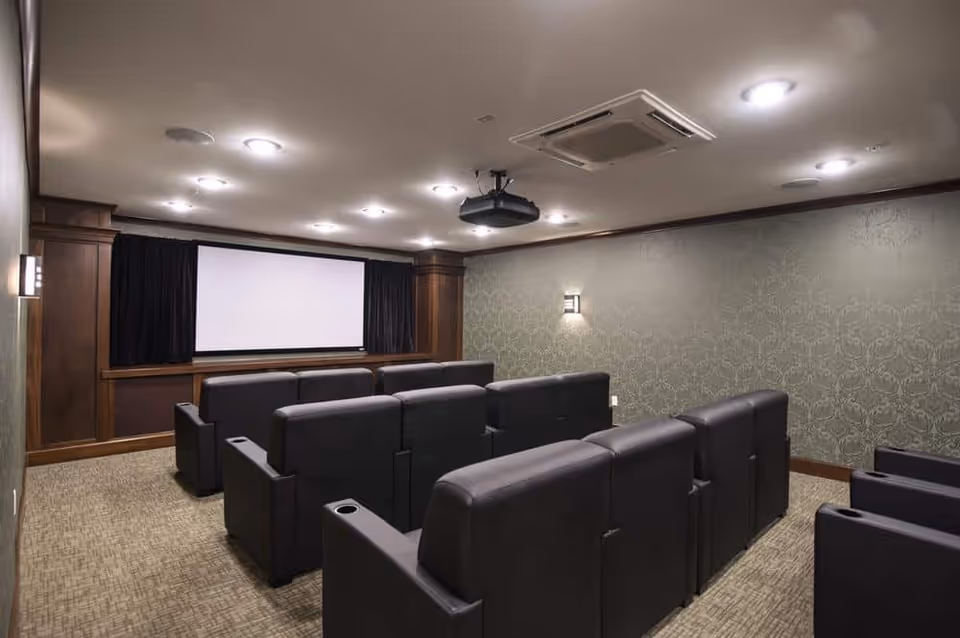 Small private theater room with rows of reclining seats facing a projection screen and ceiling-mounted projector.