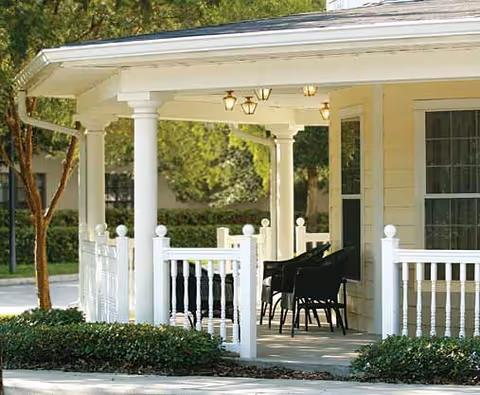 Covered front porch with white columns and railings, outdoor chairs, and light yellow siding.