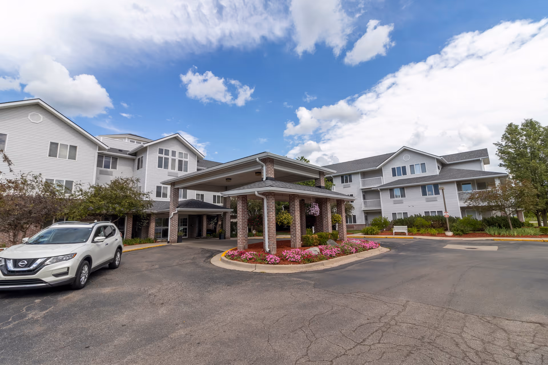 StoryPoint East Lansing senior living building exterior with covered entrance and flower bed landscaping.
