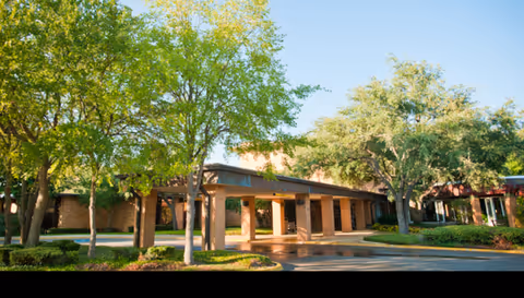 Exterior view of a senior living facility entrance with a covered drop-off and trees.