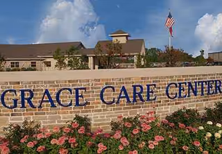 Exterior sign for Grace Care Center on brick wall with blooming flowers.