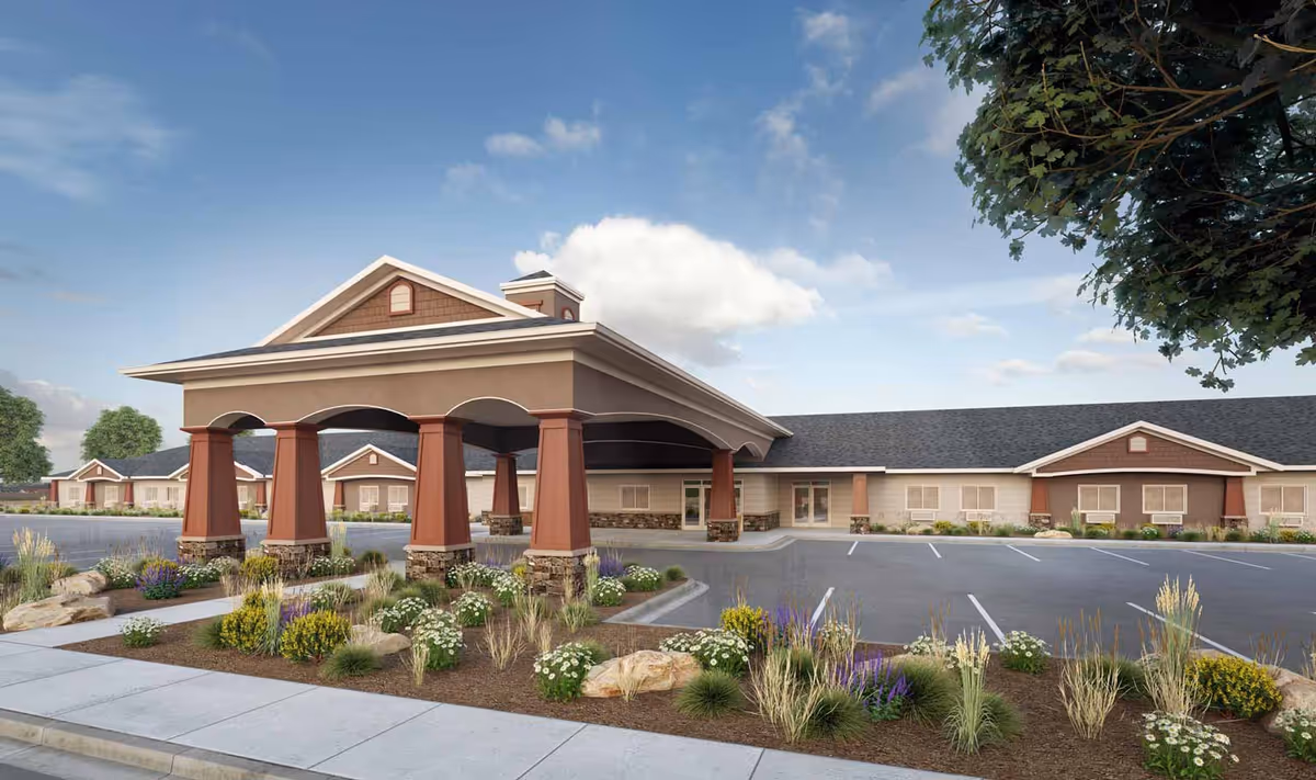 Exterior view of Aspen Creek Senior Living facility showing a covered entrance with large pillars, landscaped garden beds with various plants and flowers, a parking lot, and a long single-story building under a partly cloudy sky.
