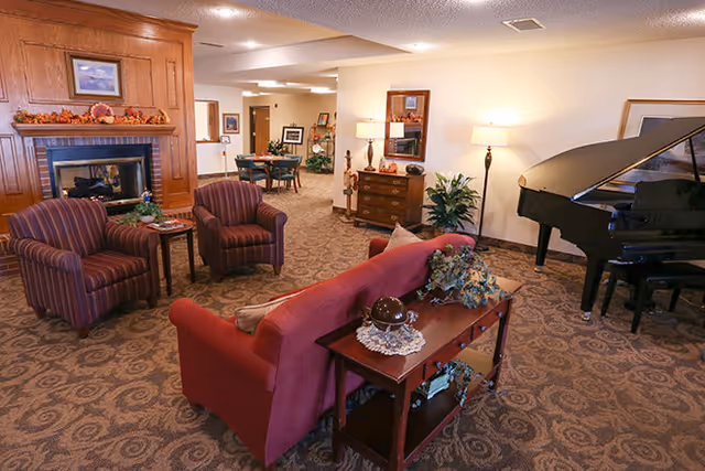 Communal living room with sofas and armchairs arranged around a fireplace and a grand piano.