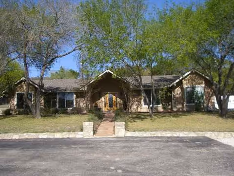Single-story brick building with a centered entrance, surrounded by trees and a paved front walkway.