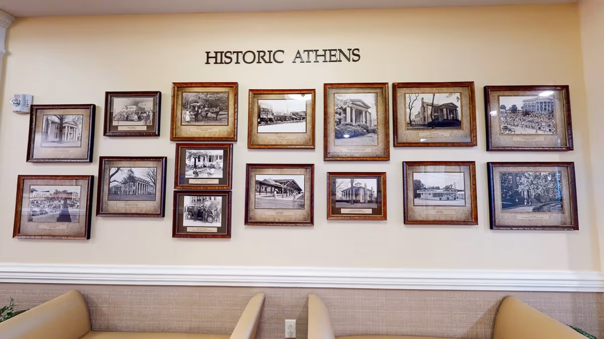 A wall display titled 'HISTORIC ATHENS' featuring fifteen framed black and white historical photographs of various buildings and scenes from Athens, arranged in three rows above beige cushioned seating.