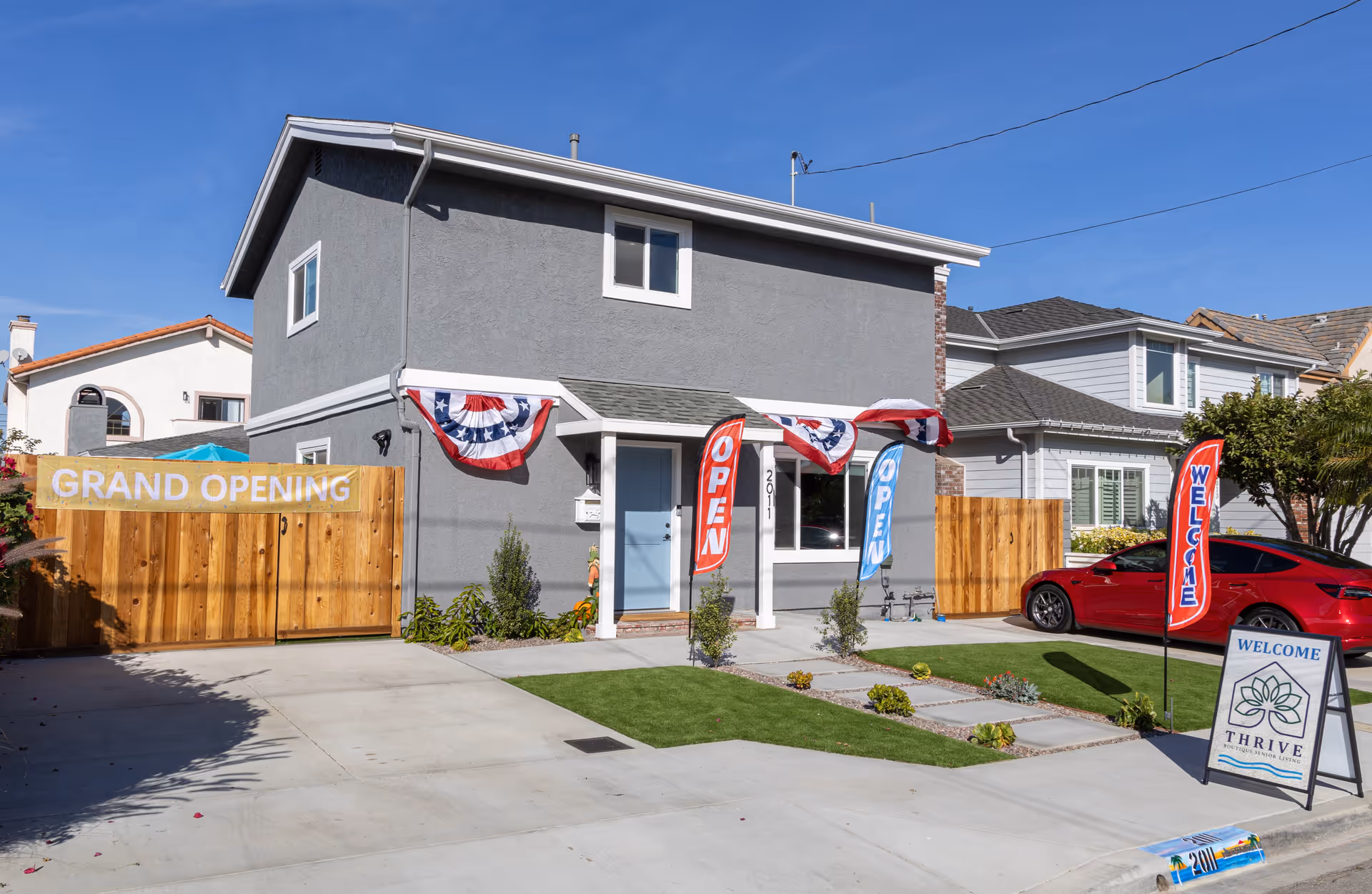 Two-story gray senior living facility with grand opening banners and welcome signs.