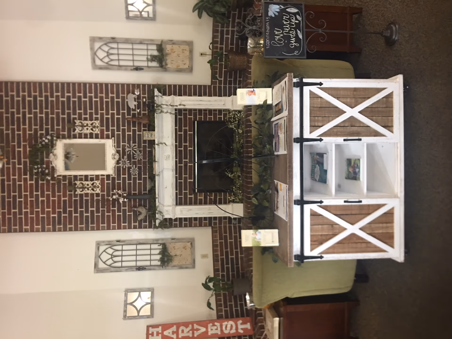 Common room with a brick fireplace, white decorative mantel, framed wall decor, and a rustic white coffee table in front of a green sofa.