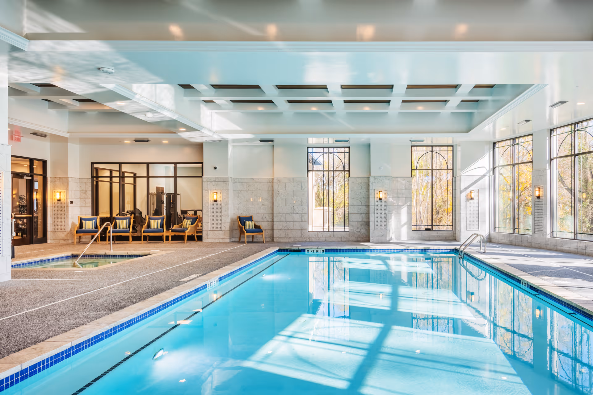 Bright indoor swimming pool with lounge seating and large arched windows letting in sunlight.