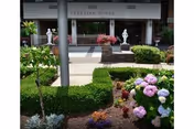 Exterior view of Teresian House entrance with statues and colorful garden flowers.