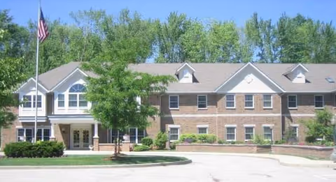 A brick senior living facility front entrance with a flagpole and trees.