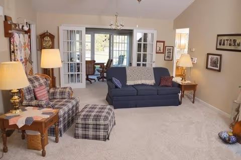 Cozy living room with plaid chair, blue sofa, and French doors to a sunlit adjoining room.