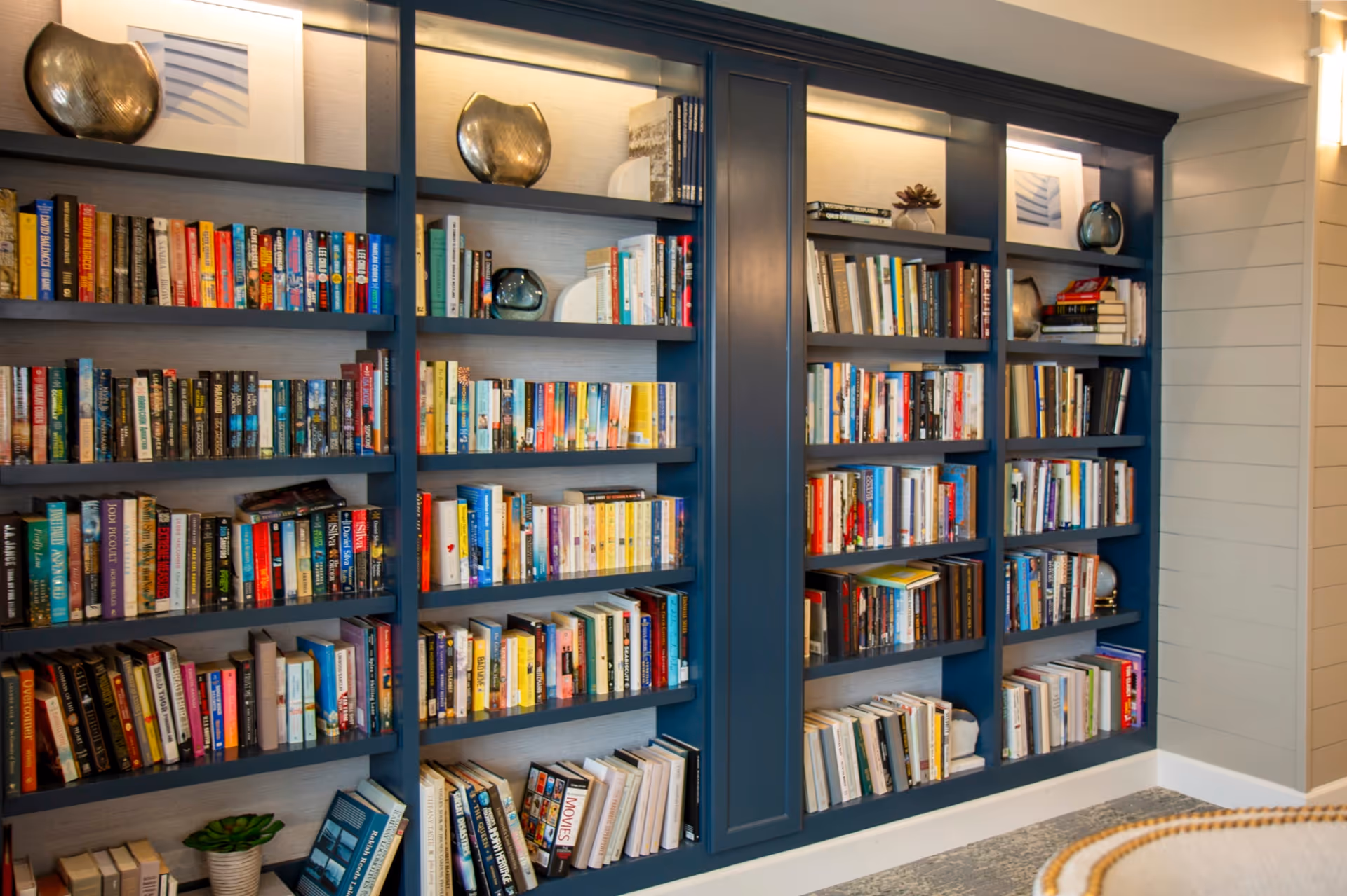 A built-in dark blue bookshelf filled with a variety of books and decorative items such as vases and framed pictures, set against a light-colored wall in a well-lit room.