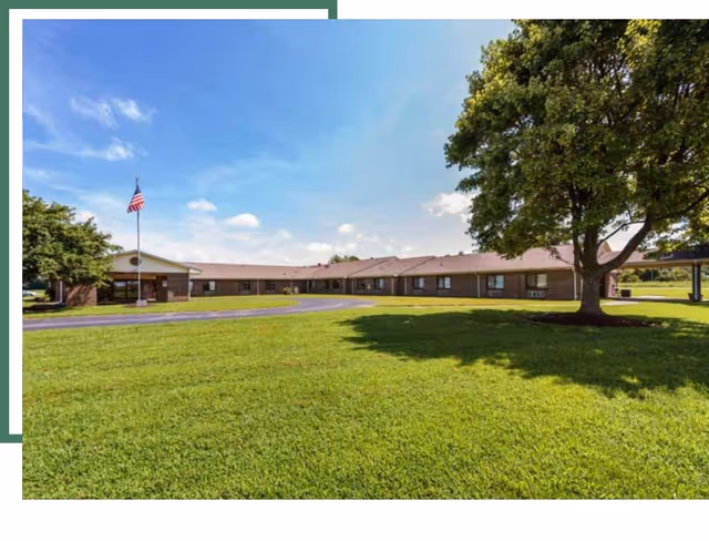 Front view of a single-story brick senior care facility with lawn and flagpole.