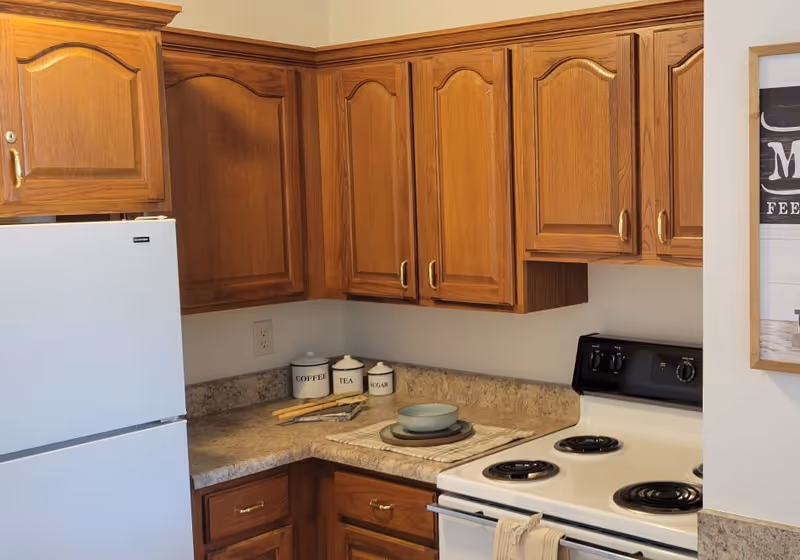 Corner kitchen with oak cabinets, a white refrigerator and electric stove, and countertop canisters and dishes.