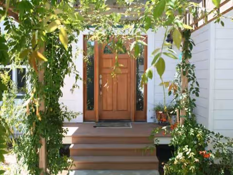 Wooden front door with steps and green vines framing a white building exterior.