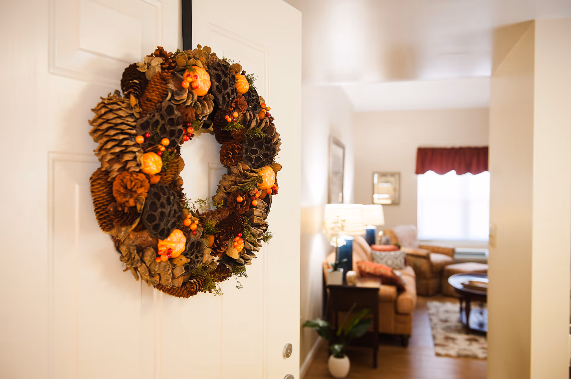 Autumn wreath hanging on an open door with a cozy living room visible beyond.