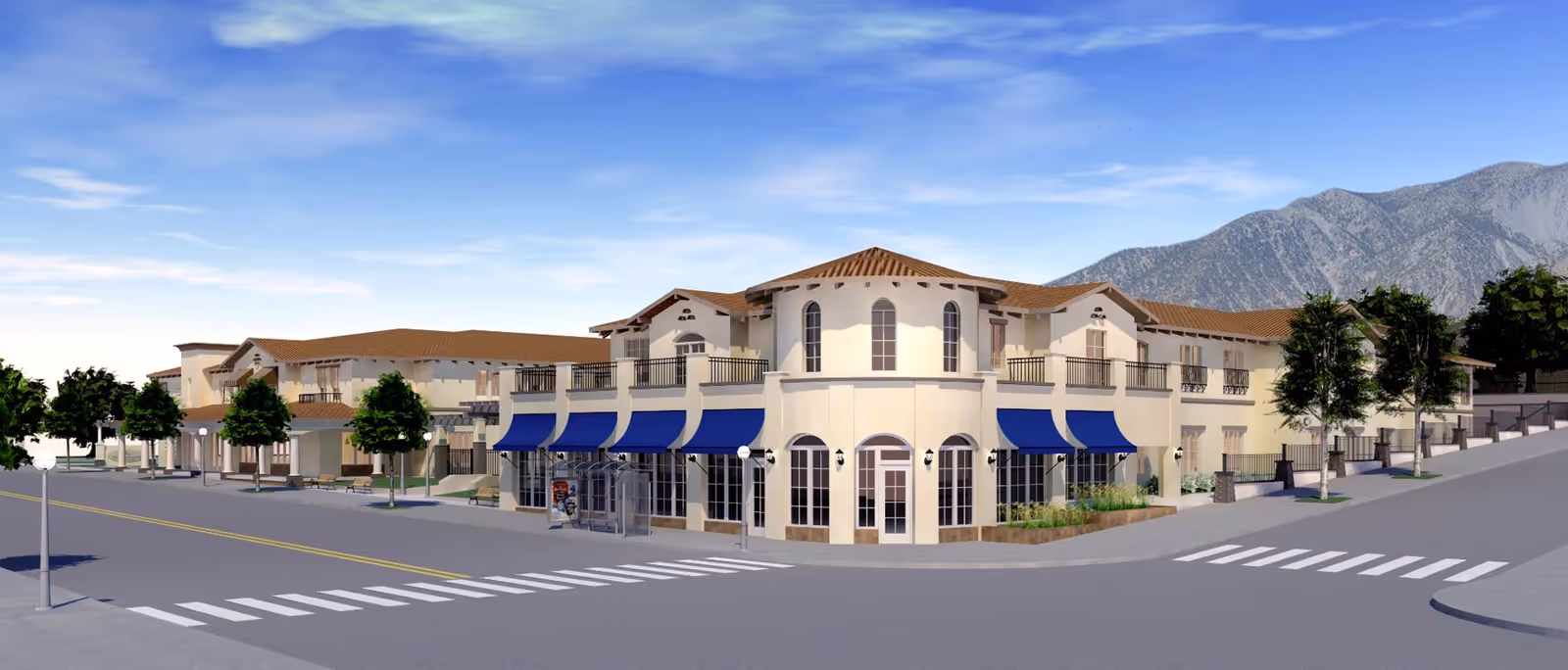 Exterior view of a two-story senior living facility building with beige walls and brown tiled roofs. The building features multiple blue awnings over windows and entrances. There are trees and landscaped areas around the building, with a mountain range visible in the background under a partly cloudy sky. A crosswalk and street are in the foreground.