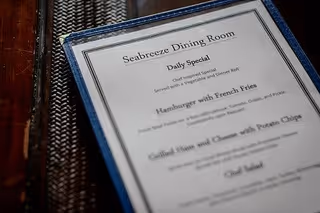 Close-up image of a menu from Seabreeze Dining Room showing the daily specials including Chef inspired Salad, Hamburger with French Fries, Grilled Ham and Cheese with Potato Chips, and Chef Salad.