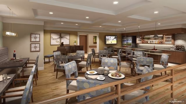 Well-lit dining and lounge area with multiple tables and upholstered chairs, a service bar, and a wall-mounted TV.