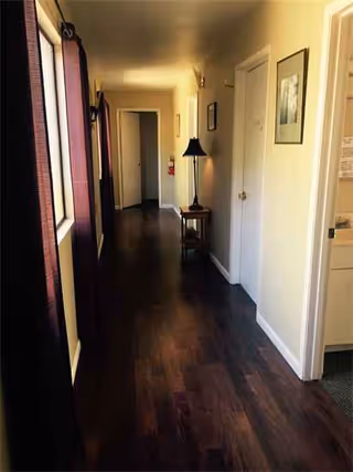 Narrow interior hallway in a senior living facility with wooden floor, doors, and a lamp.