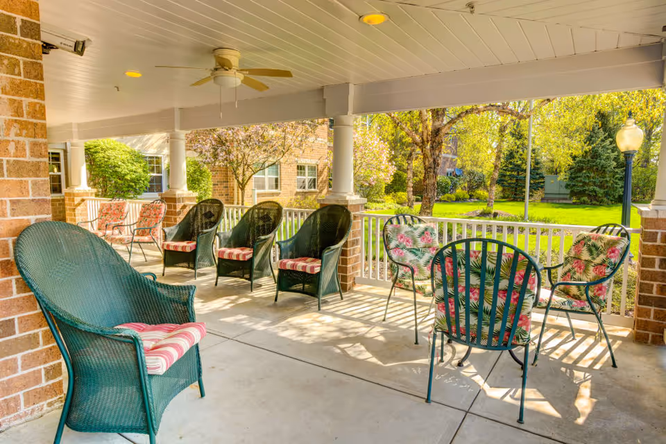 Covered outdoor porch with wicker and metal chairs with floral and striped cushions overlooking a sunny courtyard.
