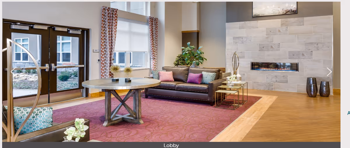 Modern lobby with a round table, leather sofa, decorative pillows, area rug, and a built-in fireplace.