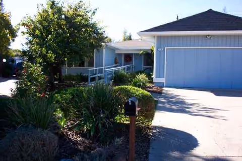 Blue single-story senior living home exterior with driveway, garden, and front entrance.