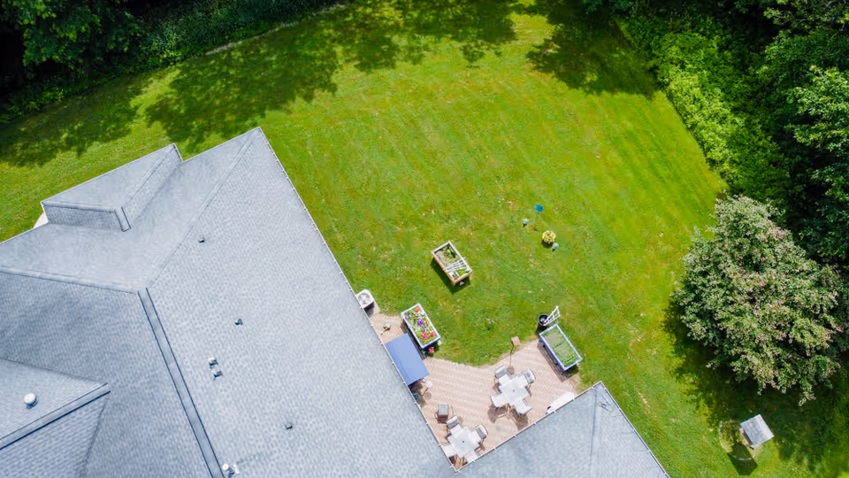 Aerial view of a senior living facility's outdoor patio area with tables and chairs, surrounded by a large green lawn and trees.