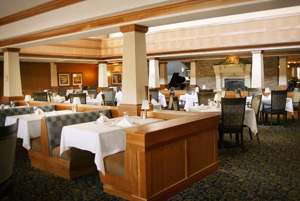 Spacious dining room with booth and table seating, white tablecloths, and a fireplace in the background.